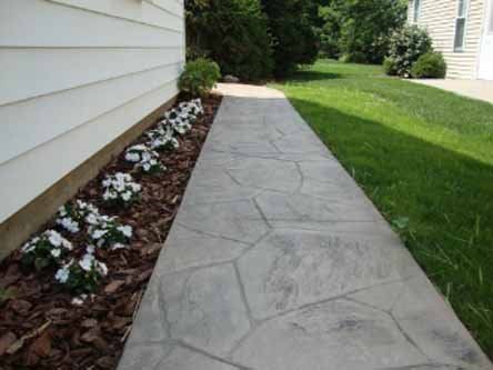 A concrete walkway leading to a house with flowers on the side.