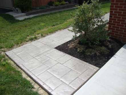 A concrete walkway leading to a brick building next to a bush.