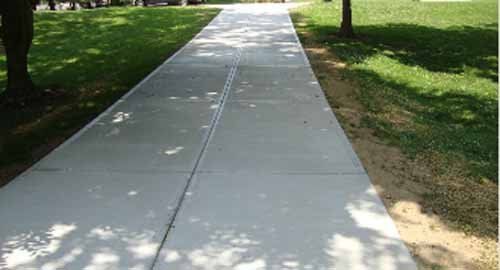 A concrete sidewalk in a park surrounded by grass and trees.