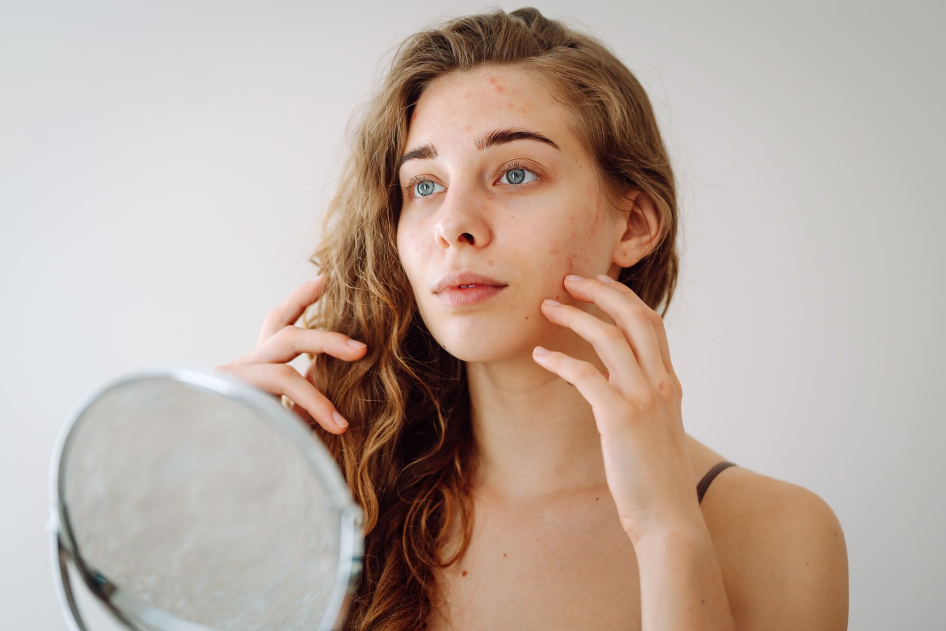 A woman is looking at her face in a mirror.