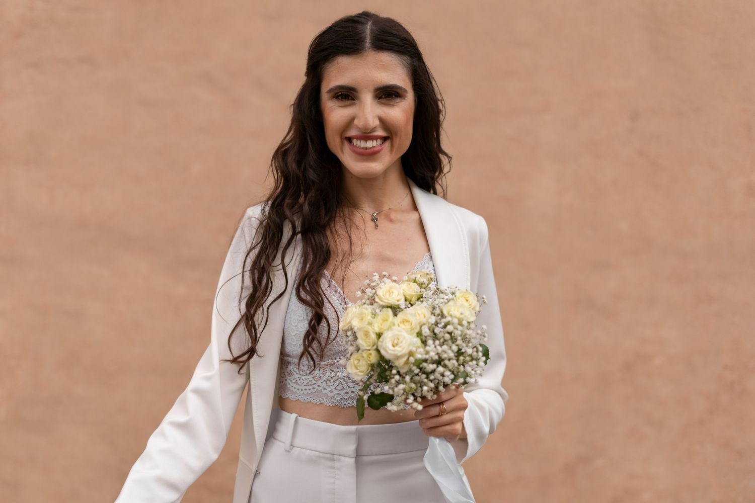 A woman in a white suit is holding a bouquet of flowers.