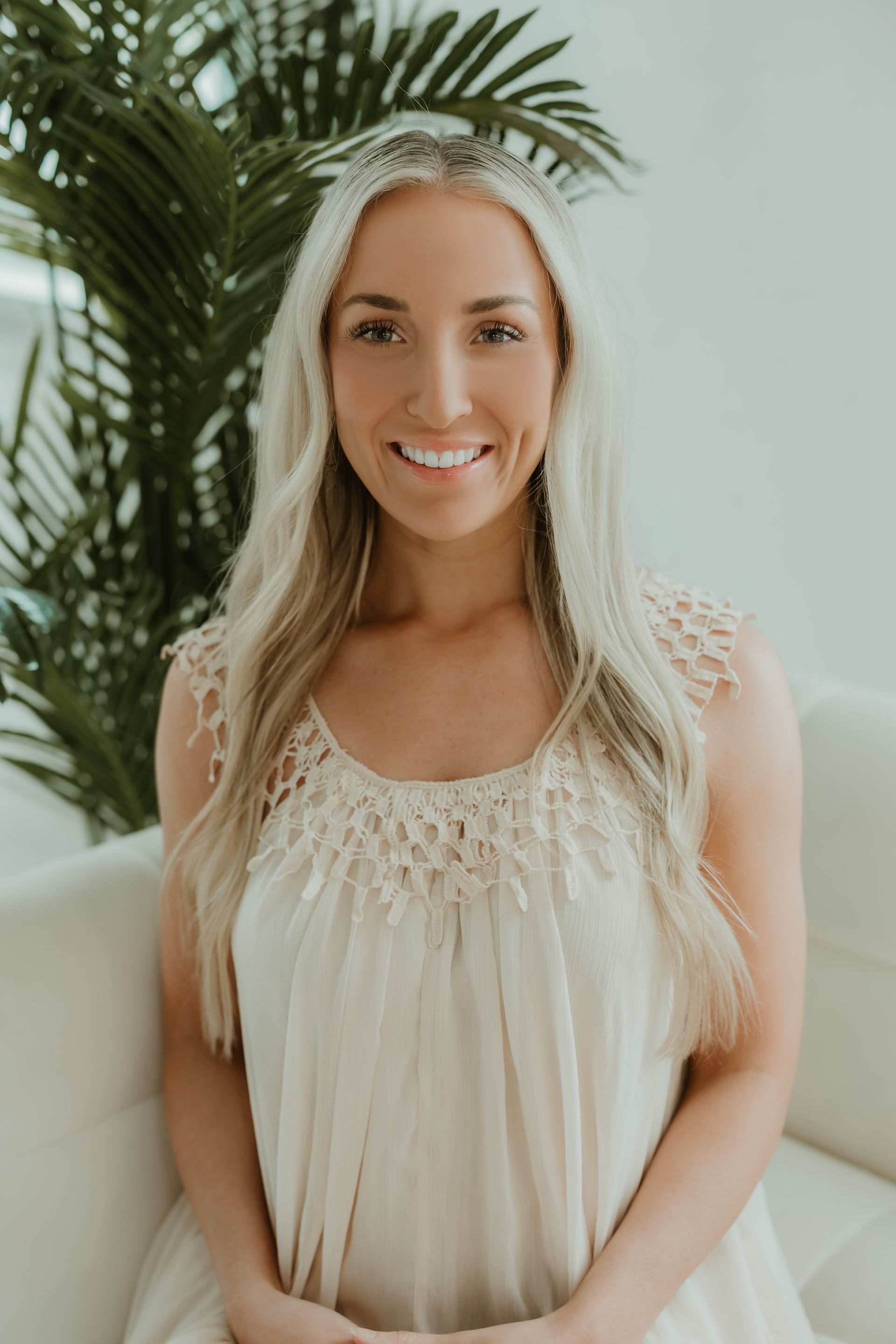 A woman in a white dress is sitting on a couch and smiling.
