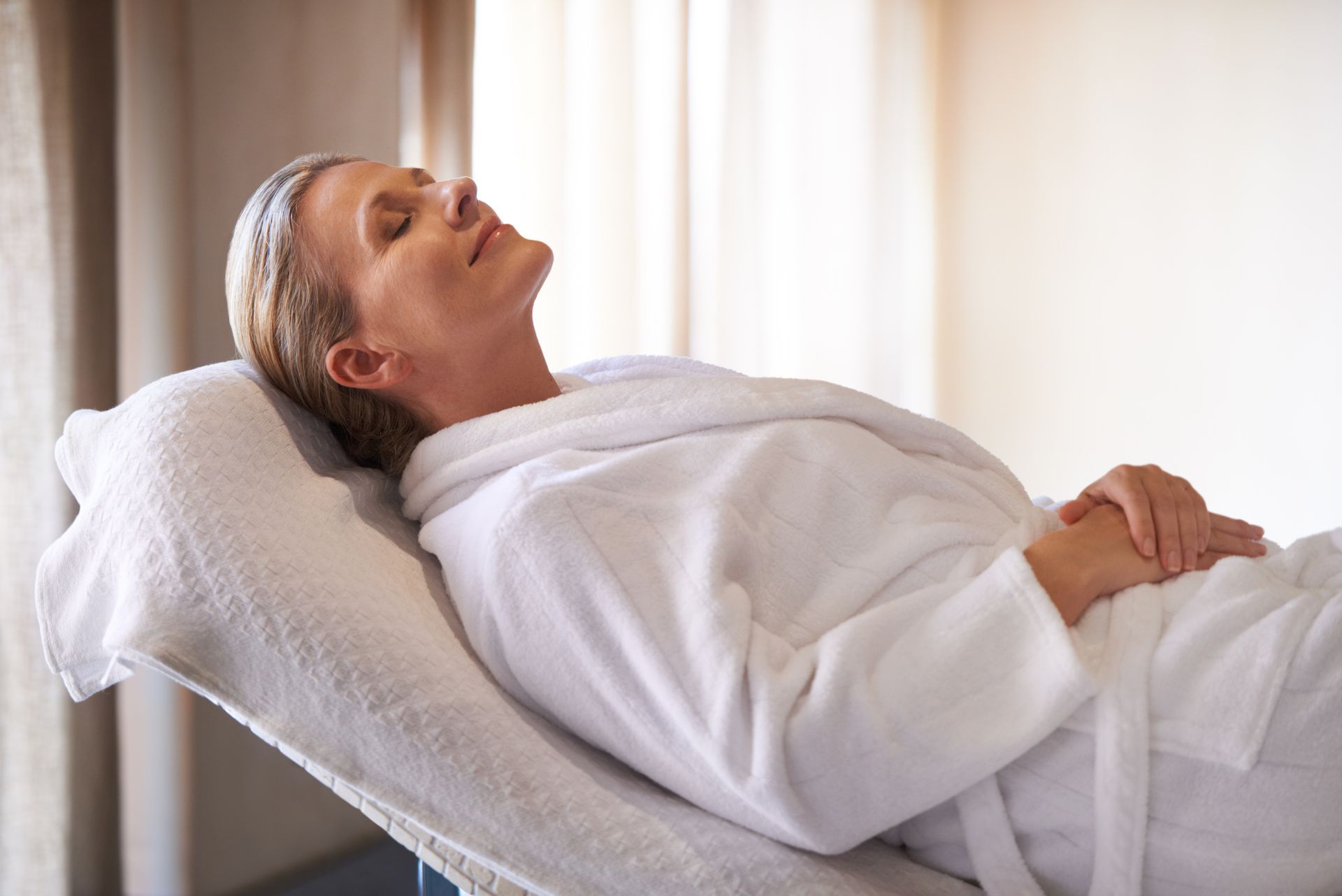 Person lying on a padded table, wearing a white robe, in a calm treatment room