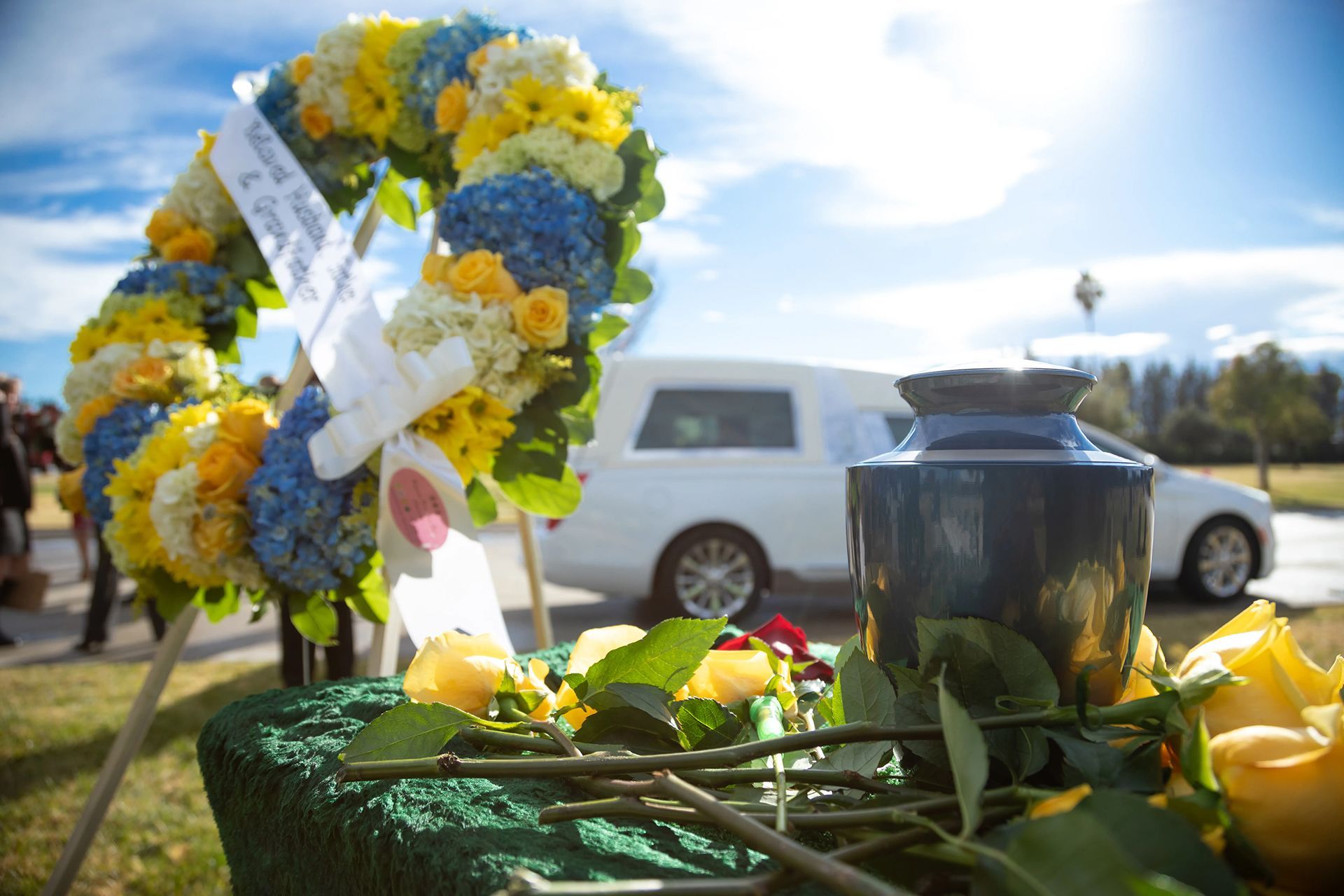 a wreath of yellow and blue flowers sits in front of a funeral car