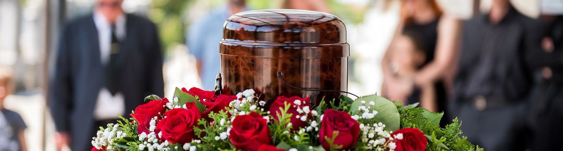 a urn is surrounded by red roses and baby 's breath at a funeral .