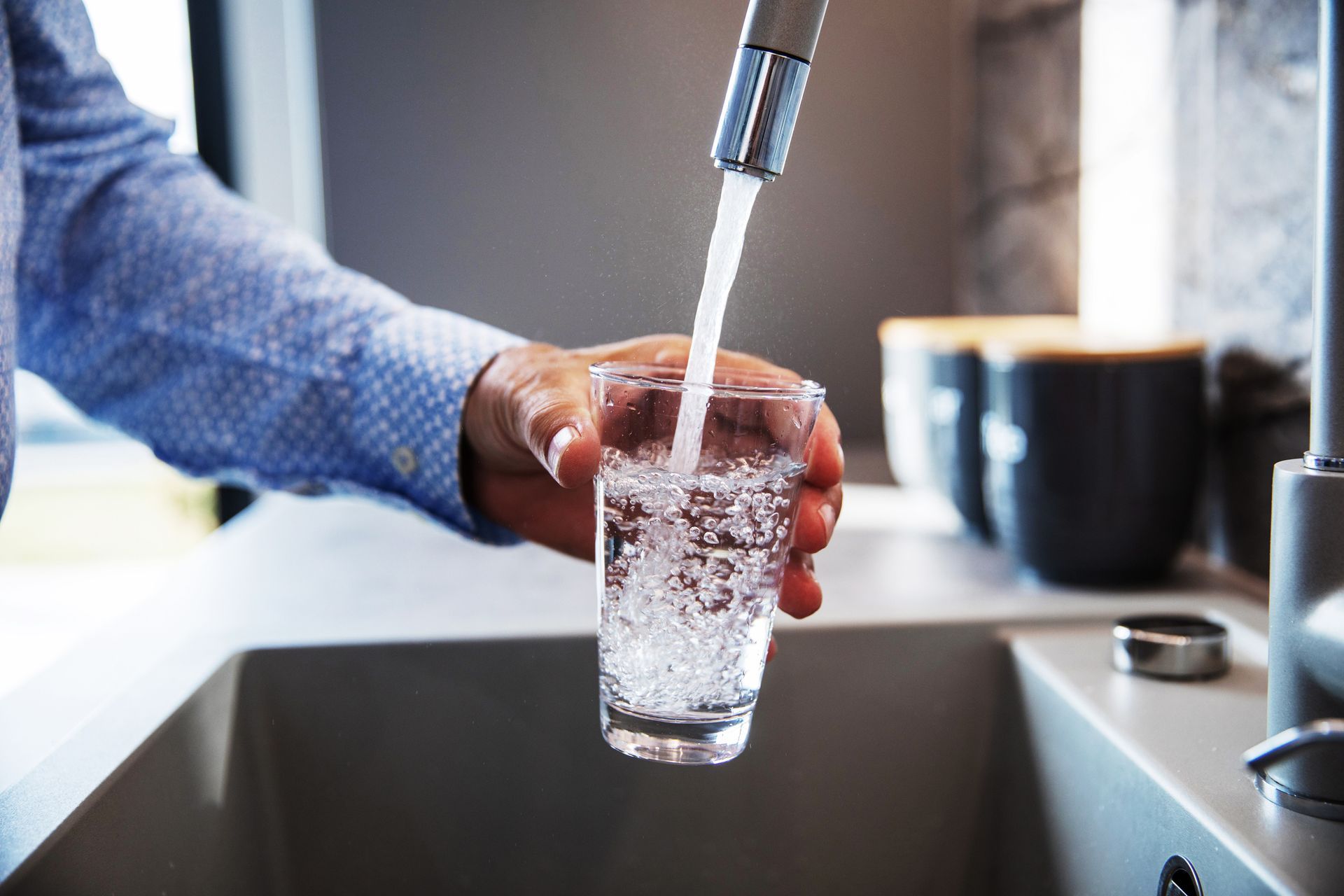 Person filling a glass with water from a kitchen faucet.