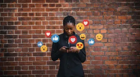 Une femme se tient devant un mur de briques et regarde son téléphone.