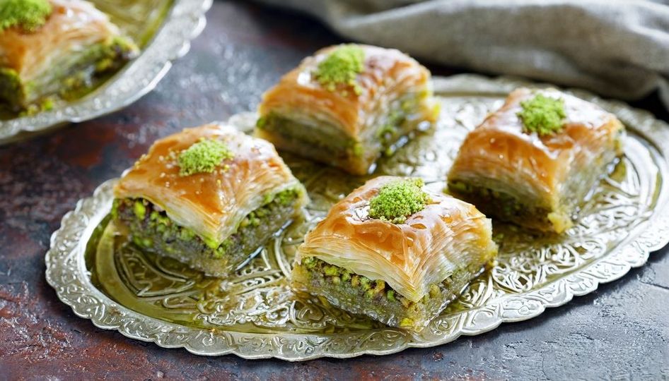 A tray of baklava with pistachios on top on a table.