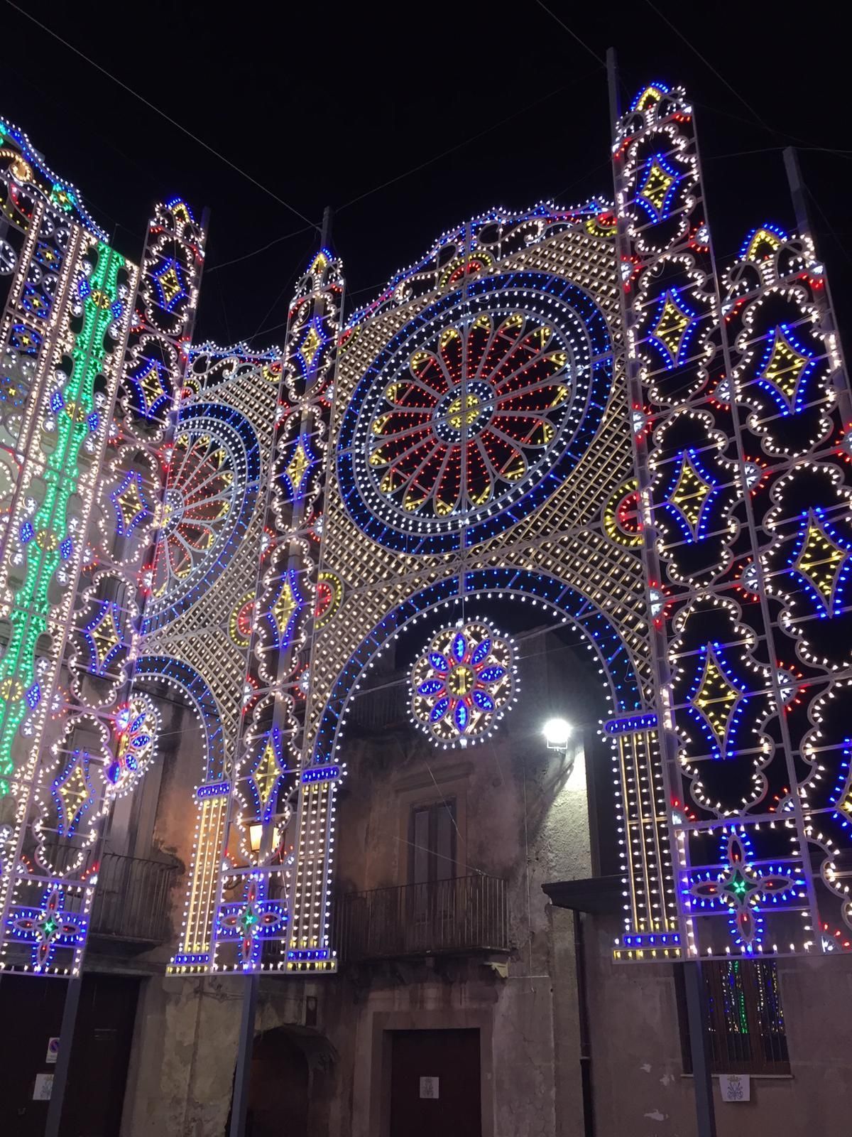 Veduta notturna della facciata di un edificio decorata con luci festive colorate e motivi circolari.