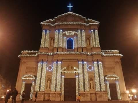 Facciata della chiesa illuminata di notte con una croce illuminata di blu e luci decorative sugli archi e sulle colonne.