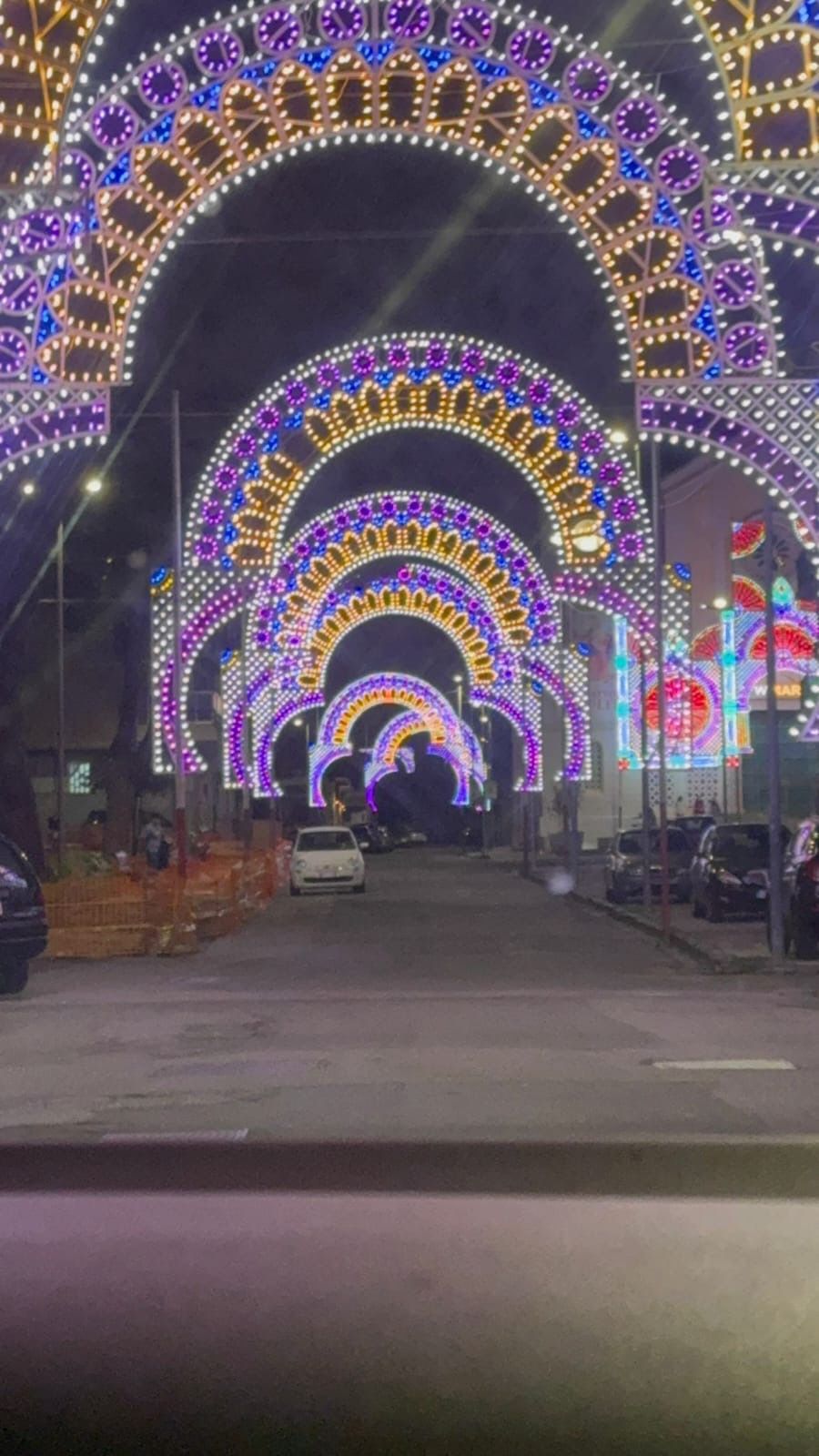 Strada notturna con archi illuminati di viola, oro e bianco che formano un tunnel sopra la strada.