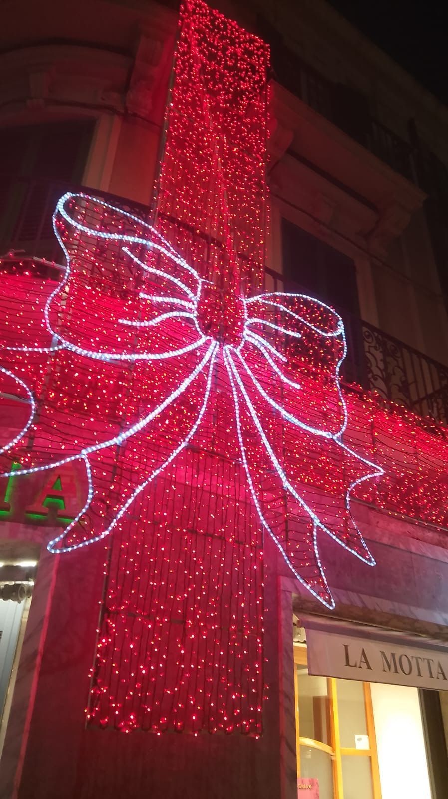 Decorazione natalizia con fiocchi rossi e bianchi sulla facciata di un edificio di notte.