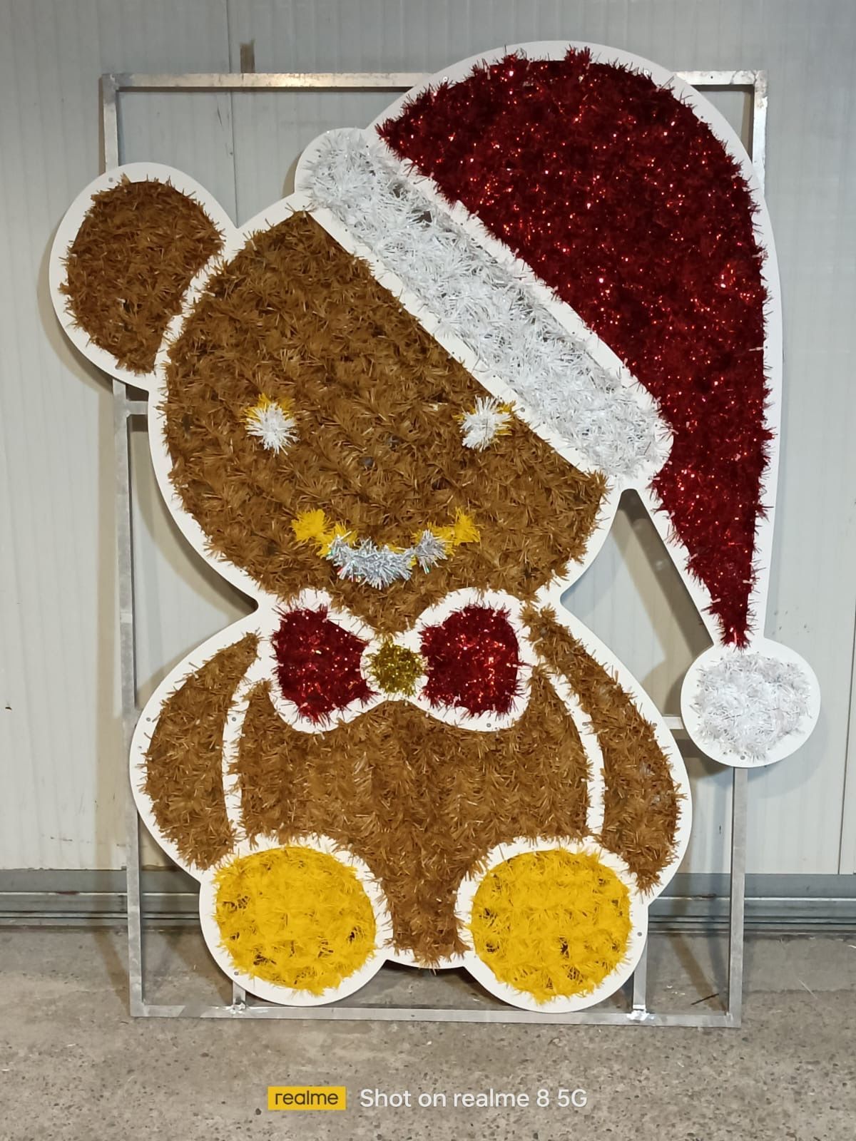 Decorazione natalizia a forma di orsetto con cappello di Babbo Natale rosso, papillon e bottoni gialli su una struttura in metallo.