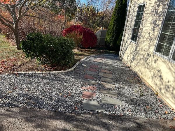 A stone walkway leading to a house with a gravel driveway.
