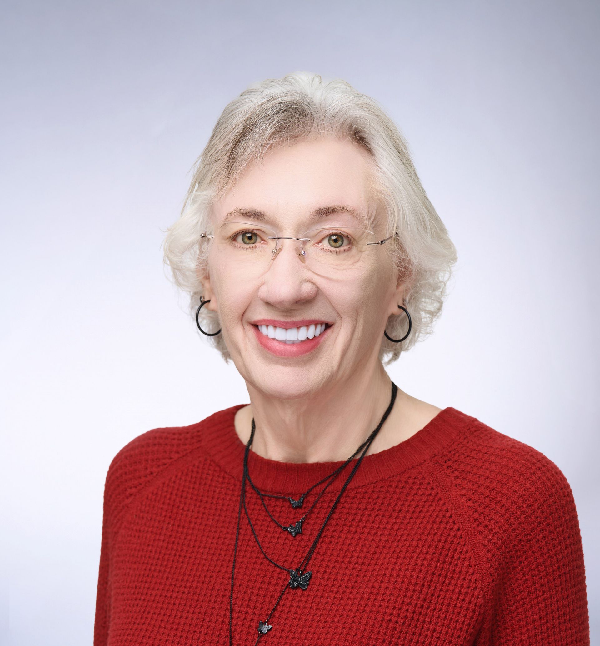 A woman wearing glasses and a red sweater is smiling for the camera.