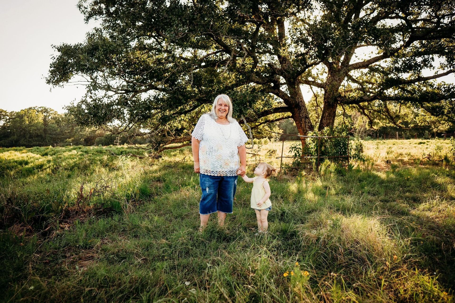 A woman and a little girl are standing in a field holding hands.