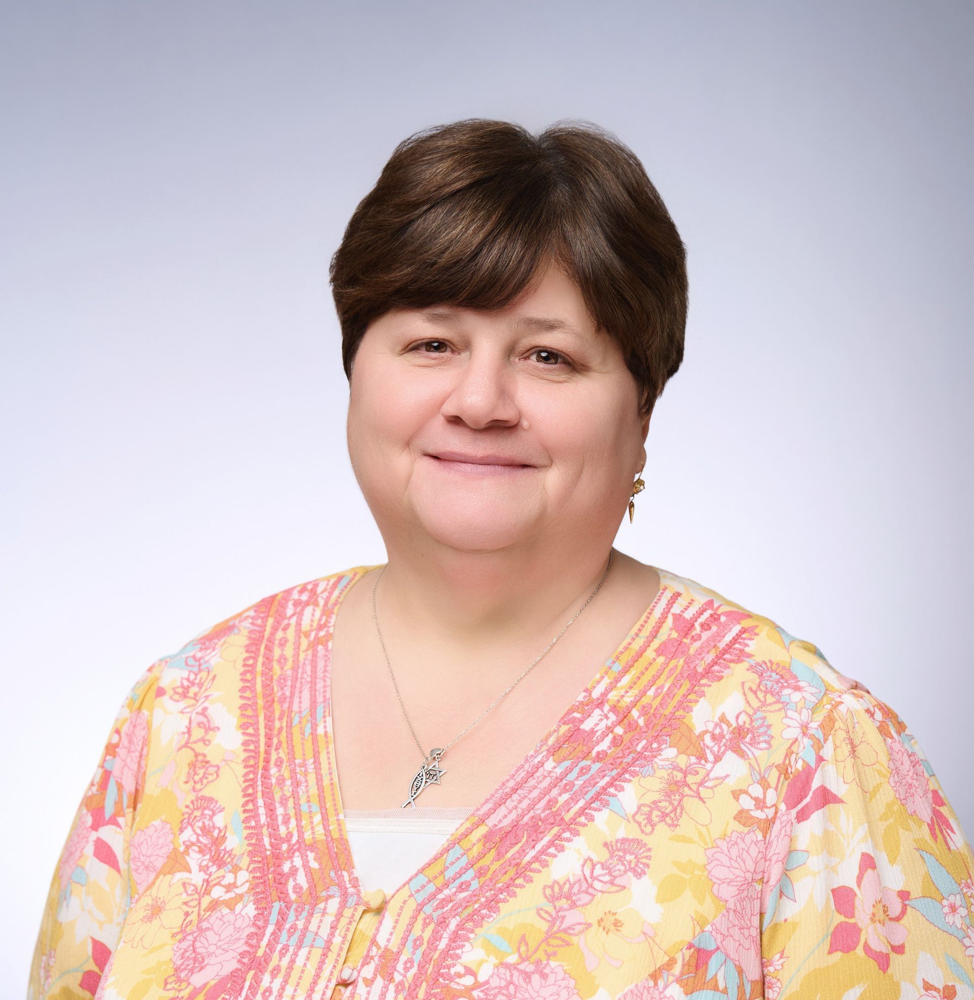 A woman in a pink and yellow floral shirt is smiling for the camera.