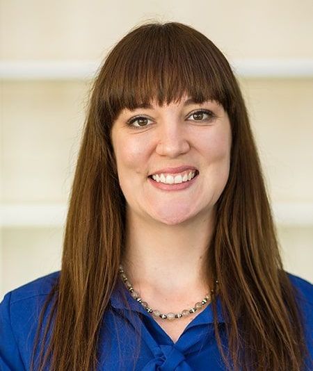 A woman wearing a blue shirt and a necklace is smiling for the camera.