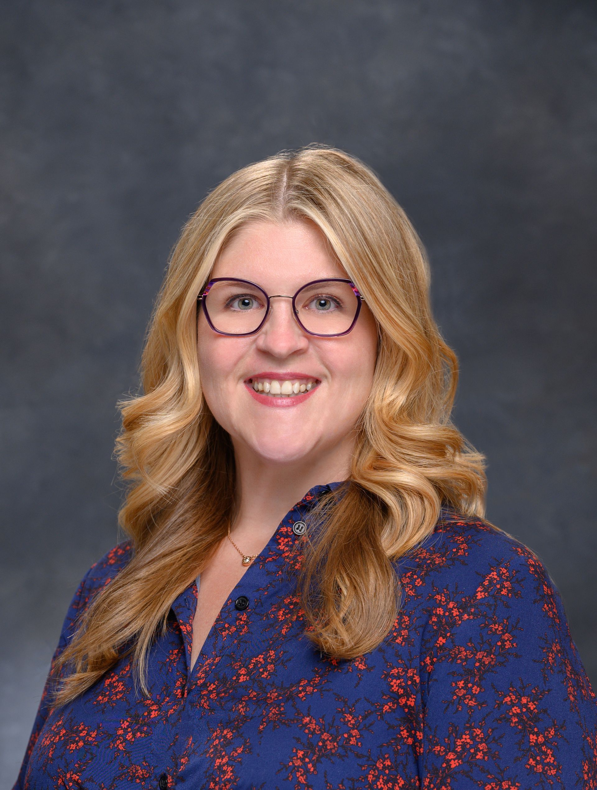 A woman wearing glasses and a blue shirt is smiling for the camera.