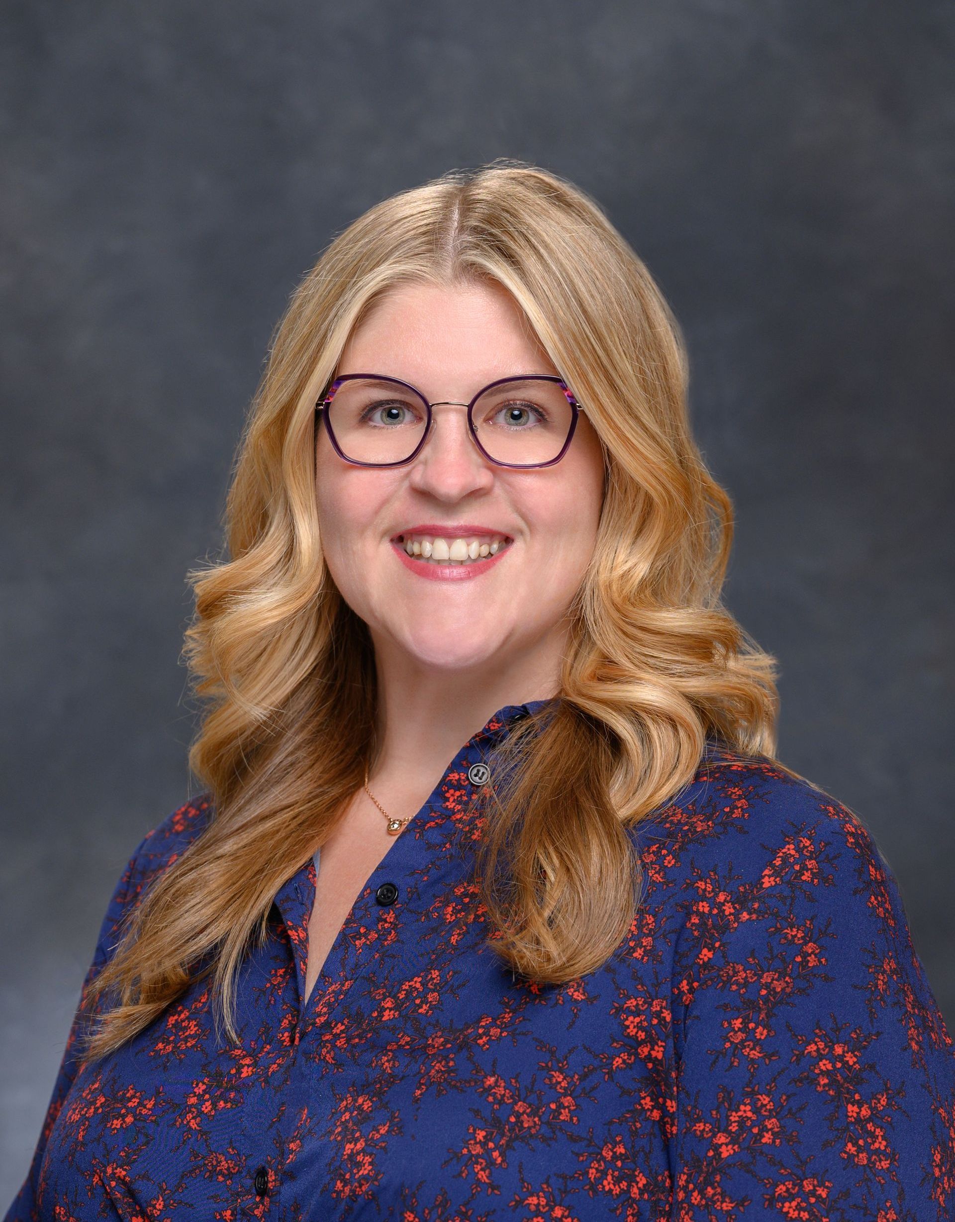 A woman wearing glasses and a blue shirt is smiling for the camera.