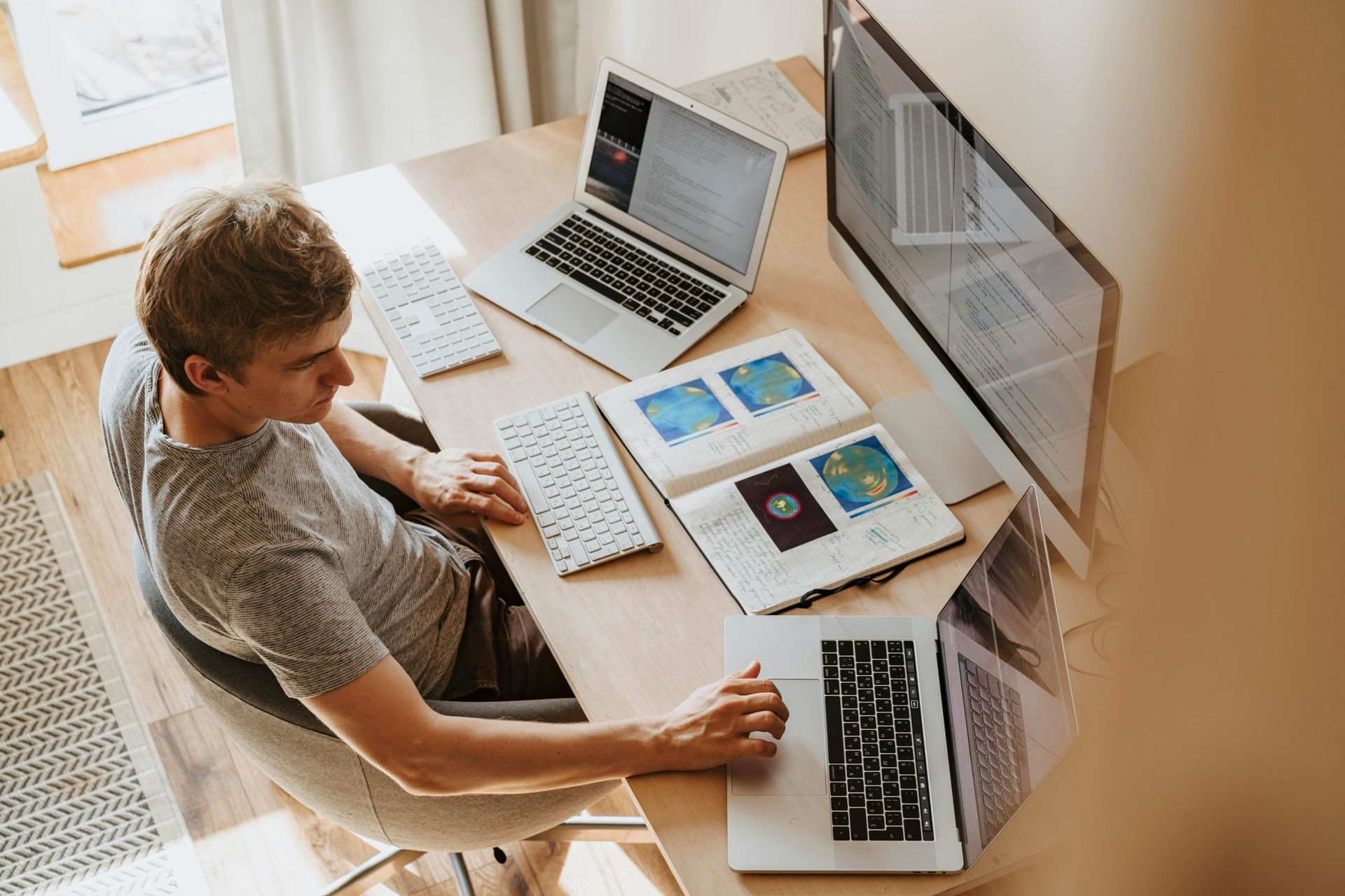 A man is sitting at a desk with two laptops and a computer.