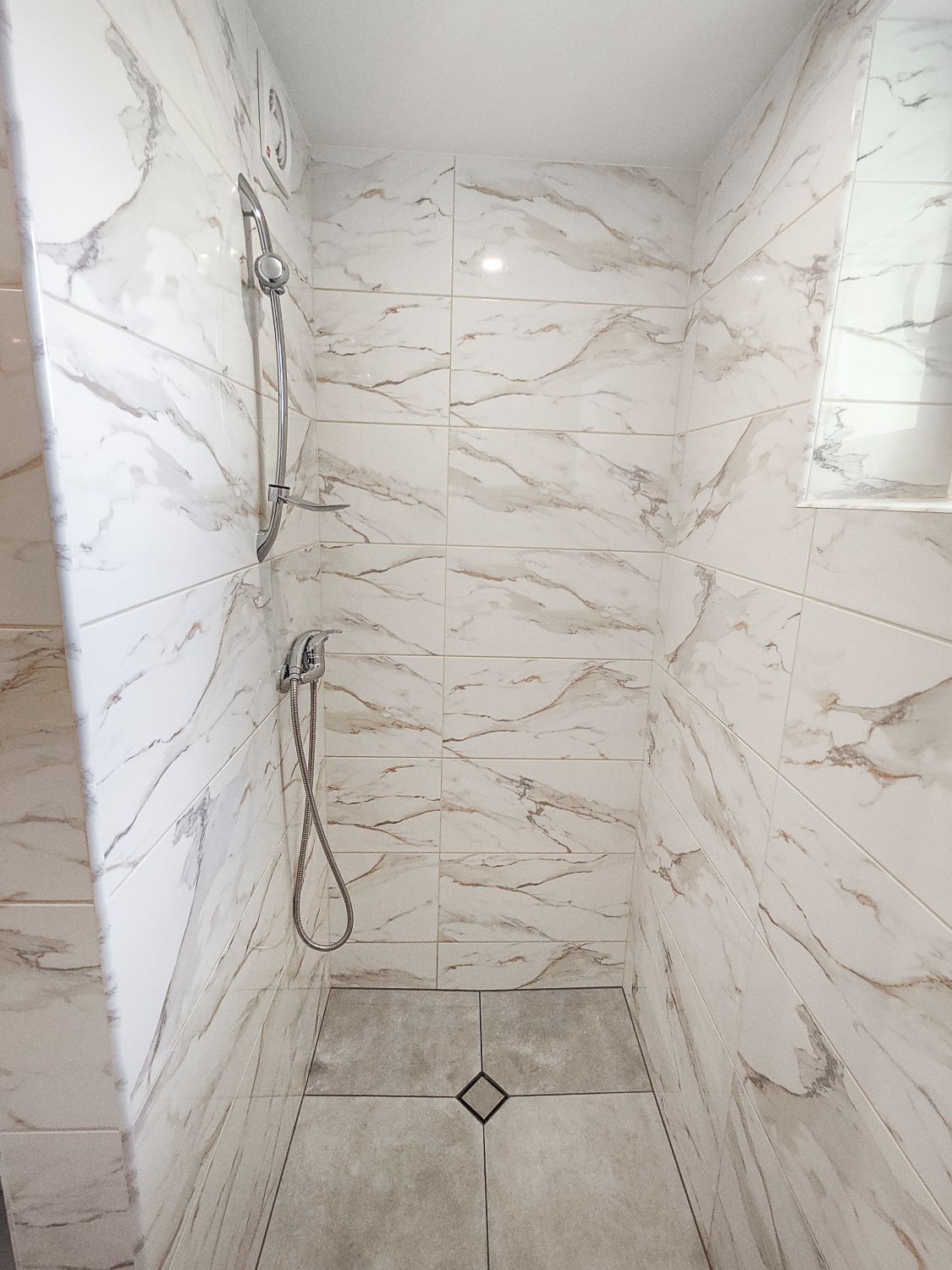 Vonios kambarys su marmurinėmis plytelėmis ir dušo kabina.