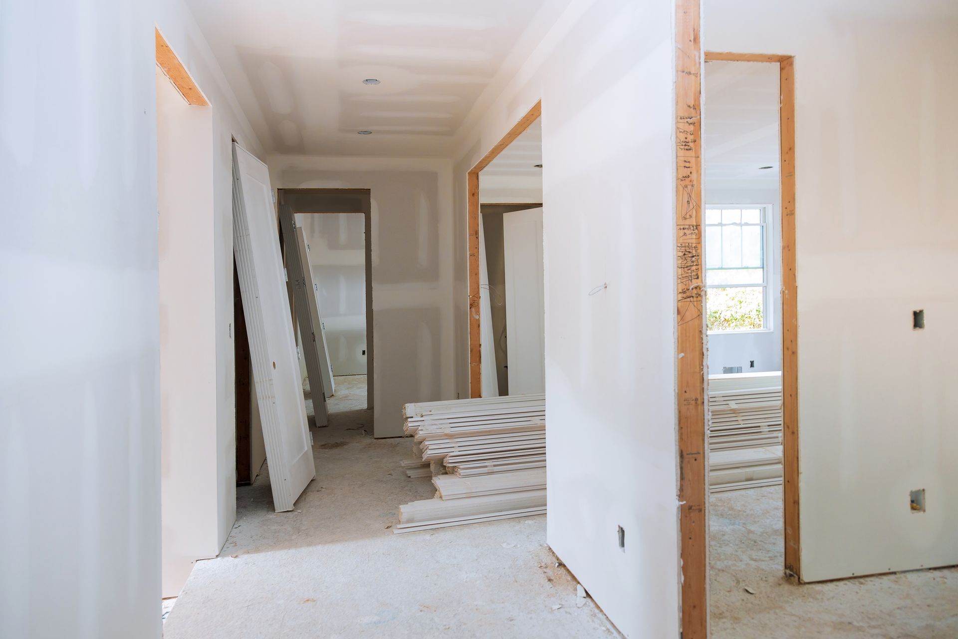 White hallway under renovation with open doorways and stacked tiles on the floor