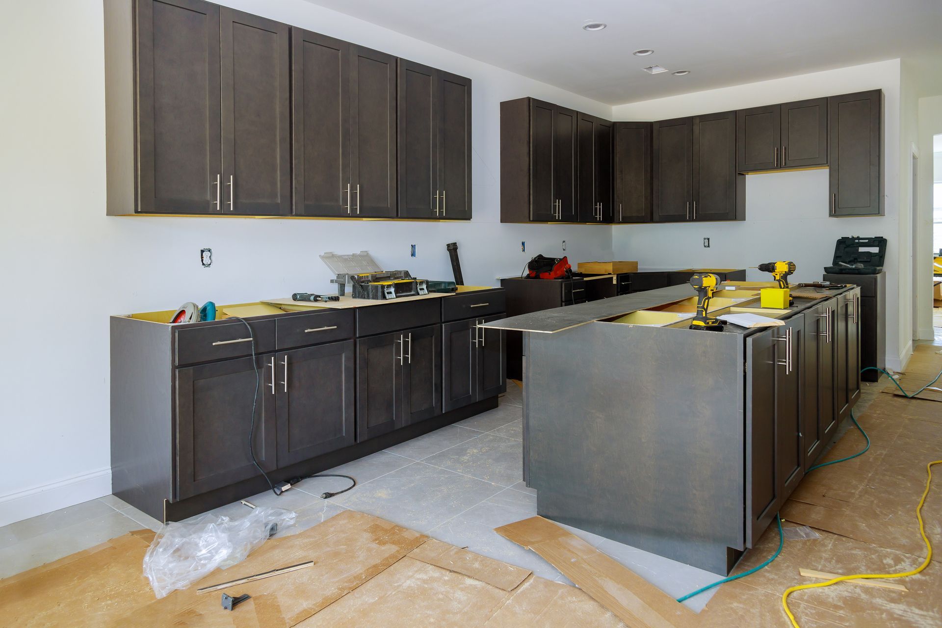 Unfinished kitchen with dark cabinets, gray island, and tools on the floor during installation