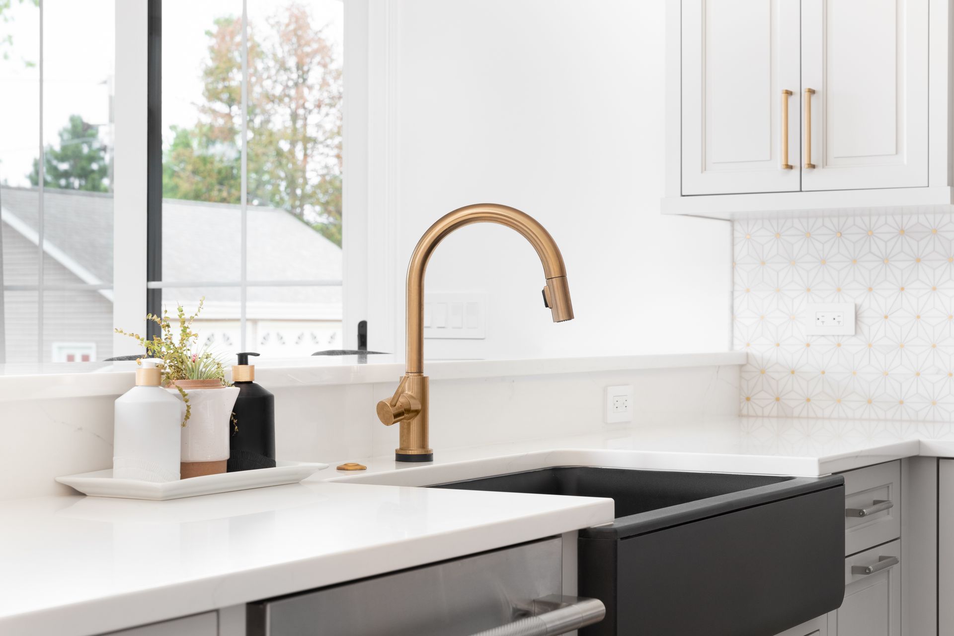 Bright white kitchen sink with gold faucet beside a black stove and window