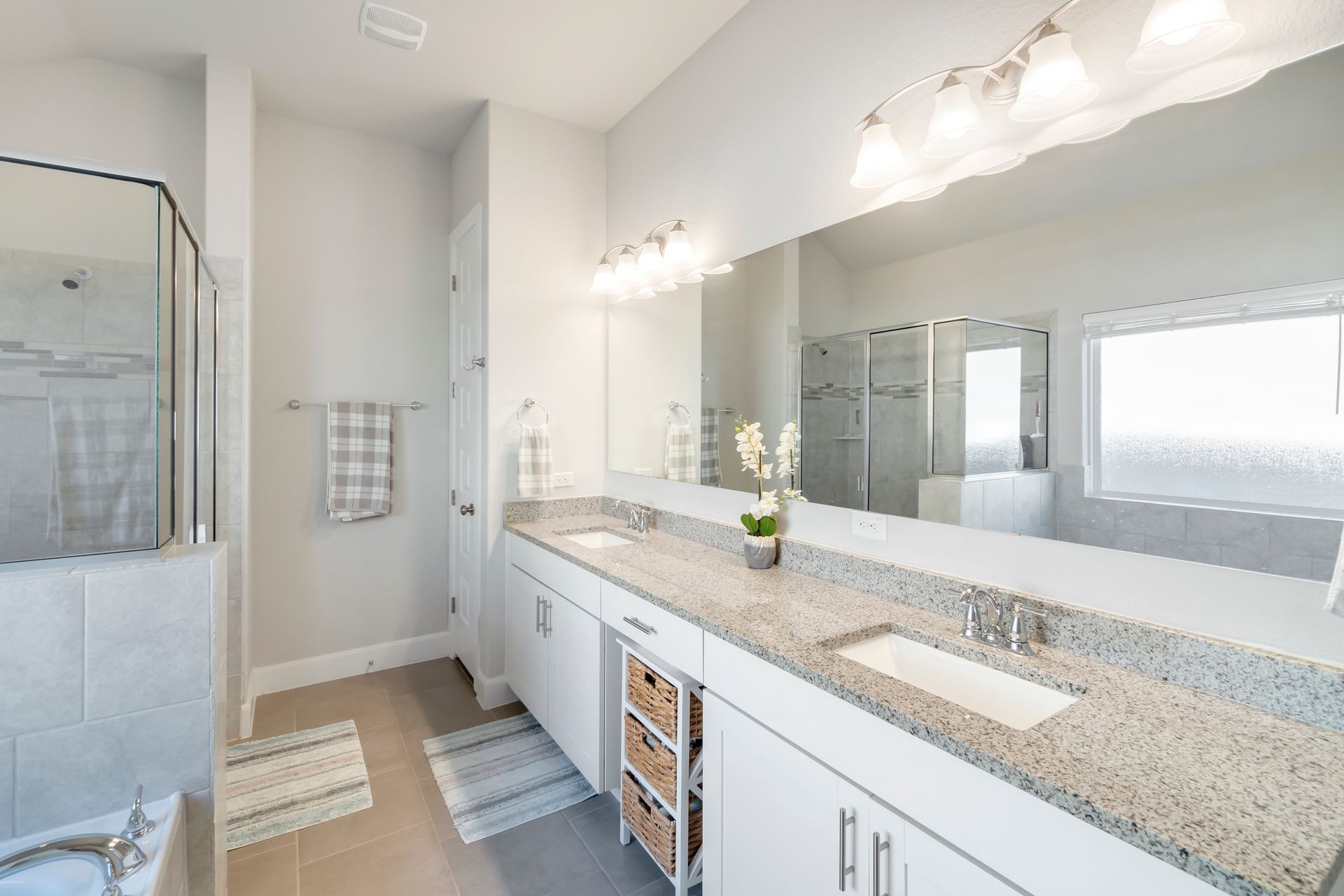 Bright modern bathroom with double vanity, large mirror, granite countertop, and glass shower.