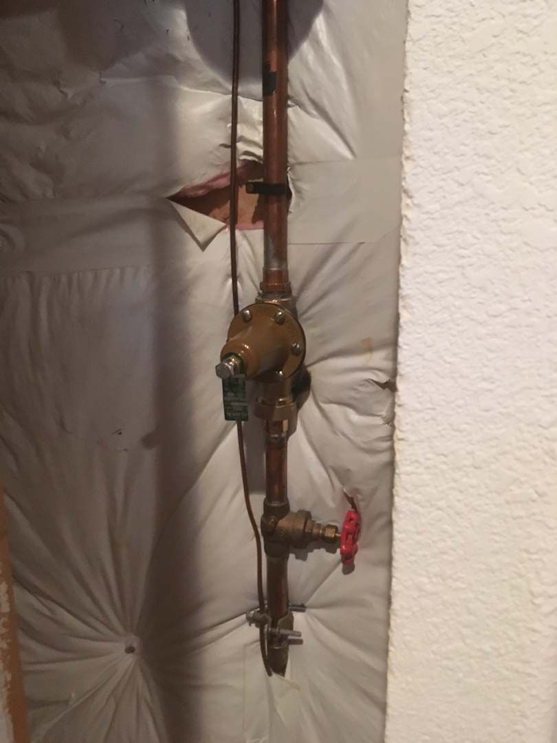 Copper pipes with a water meter and shut-off valve, mounted on insulated wall.