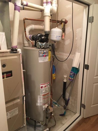 Water heater and furnace in utility closet. Plumbing pipes and expansion tank visible. Broom leaning against wall.