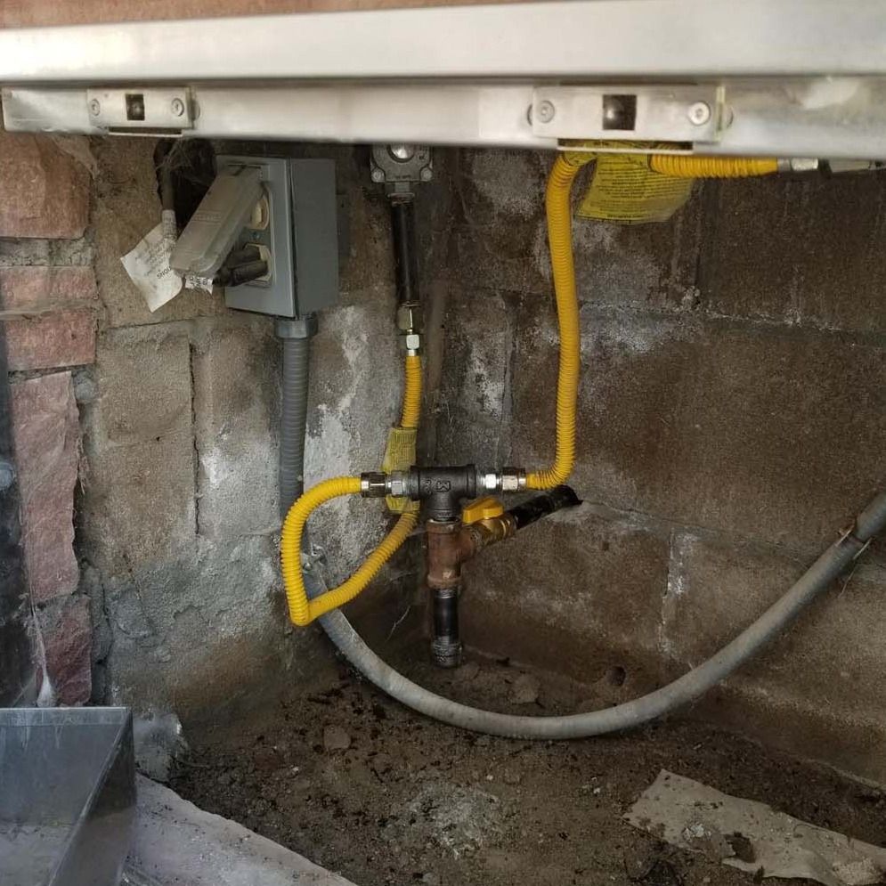 Gas pipes with yellow flexible hoses connected to a fireplace in a brick-lined alcove.