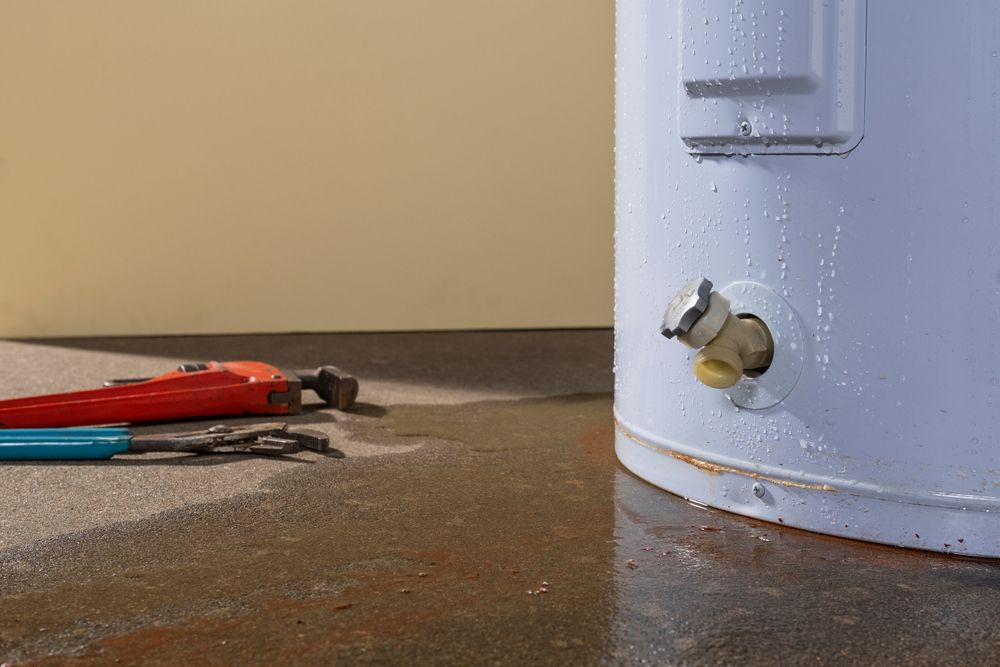 Leaking water heater with tools on a wet floor. Red and blue wrenches are next to the tank.