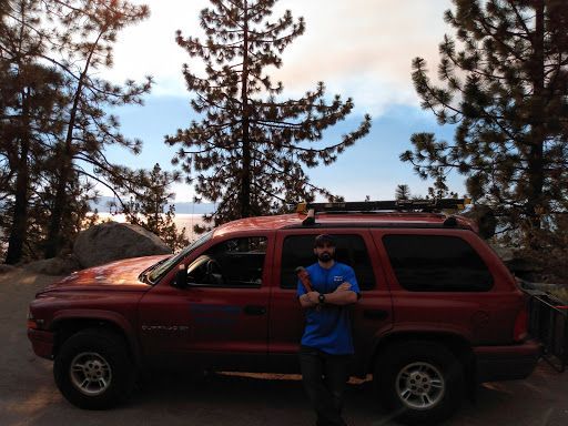 A man in a blue shirt is standing in front of a red suv.