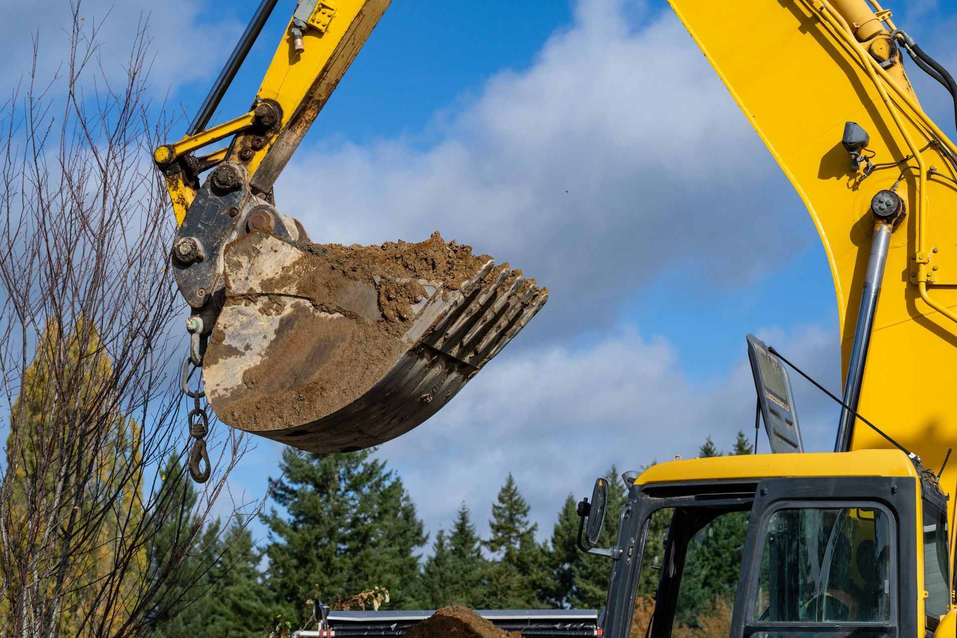 A yellow excavator hydraulic bucket lifting dirt at a construction site.