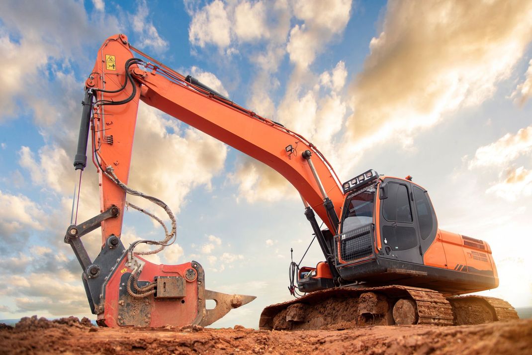 Orange excavator on a dirt construction site with large digging arm under bright cloudy sky todaynow.
