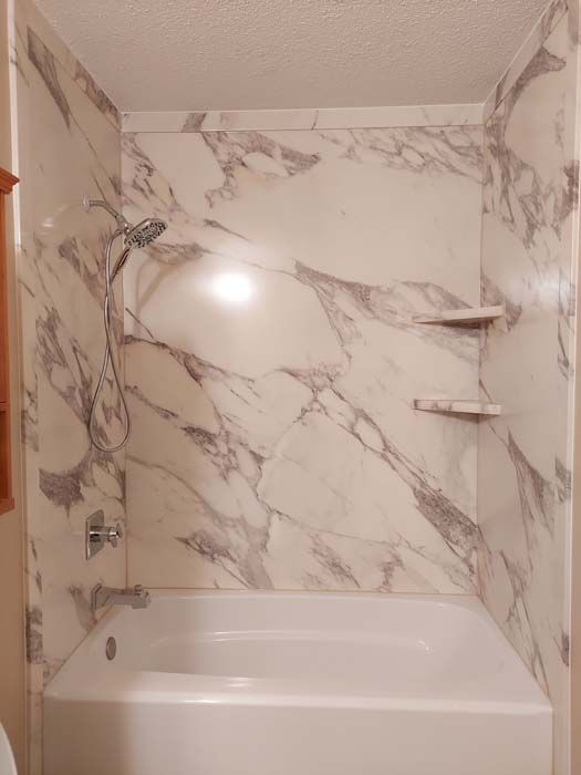 White and gray marble-patterned shower surround with built-in shelves, over a white bathtub.