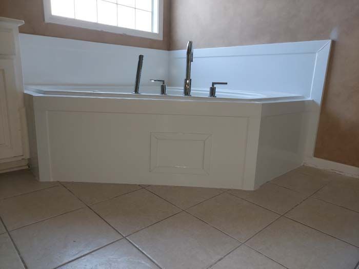 White built-in corner bathtub with tile surround and faucet fixtures in a bathroom with tiled floor.