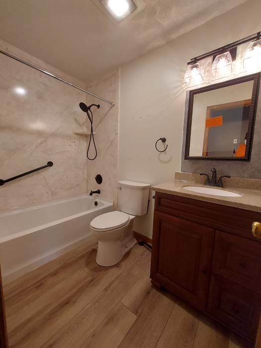 Bathroom with a tub, toilet, vanity, and shower fixtures; light brown flooring and white walls.