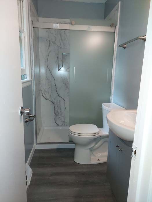 Small bathroom with a white toilet, gray flooring, shower with marble-look panel and a gray vanity.