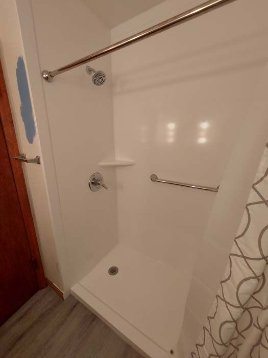 White, accessible shower stall with grab bar and showerhead.