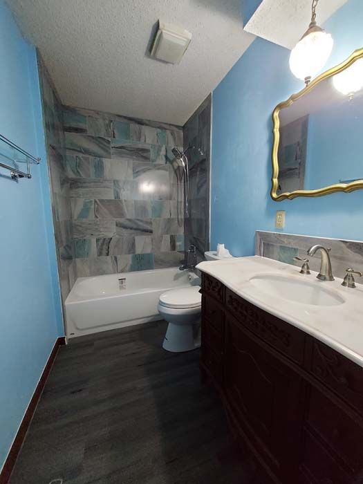 Bathroom with blue walls, marbled shower tiles, dark wood vanity, and gold-framed mirror.