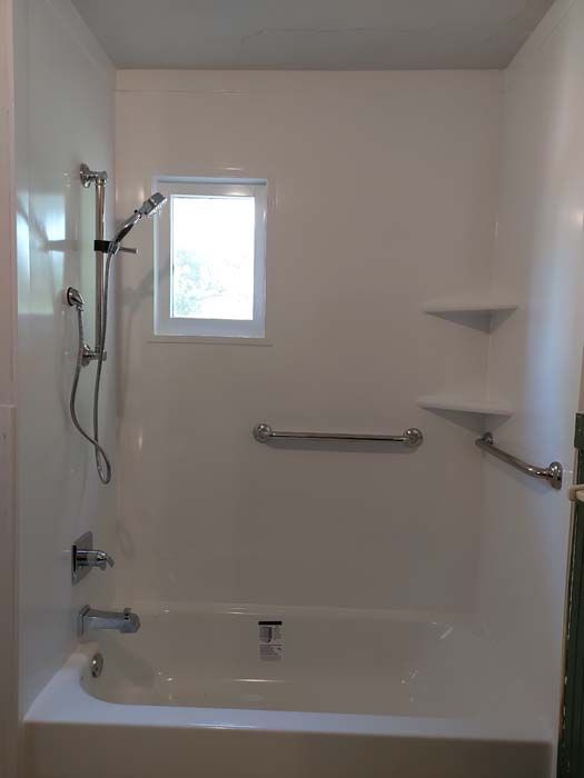 White bathroom with tub, shower, window, and grab bars.
