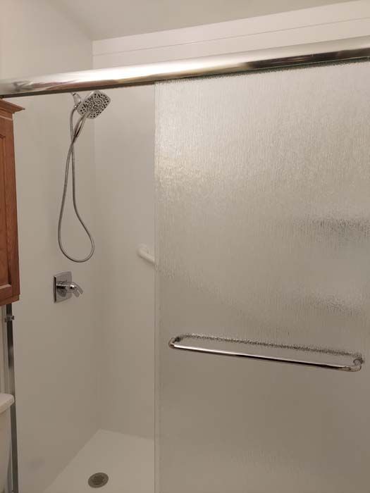 White shower stall with sliding frosted glass door, chrome fixtures, and wooden cabinet.
