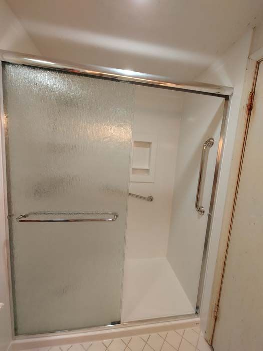 Shower stall with frosted glass doors, a grab bar, and a built-in soap dish.