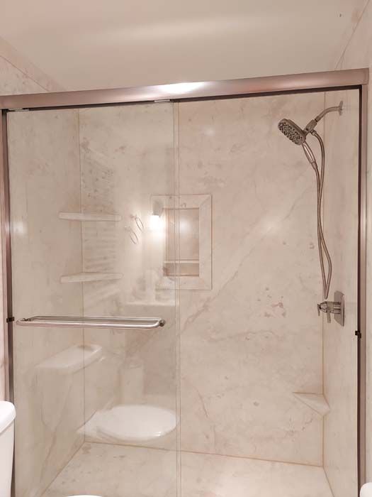 Shower stall with glass doors, marble-like walls, and a handheld showerhead.