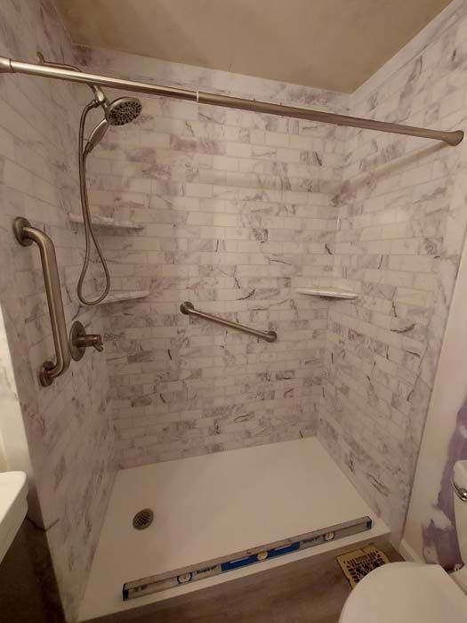 Accessible shower with grab bars, built-in shelves, and a white marble-look wall design.