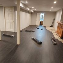 Dark flooring being installed in a room with white walls and a column. Tools are scattered about.