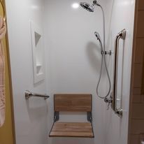Accessible shower with folding wooden seat and grab bars.